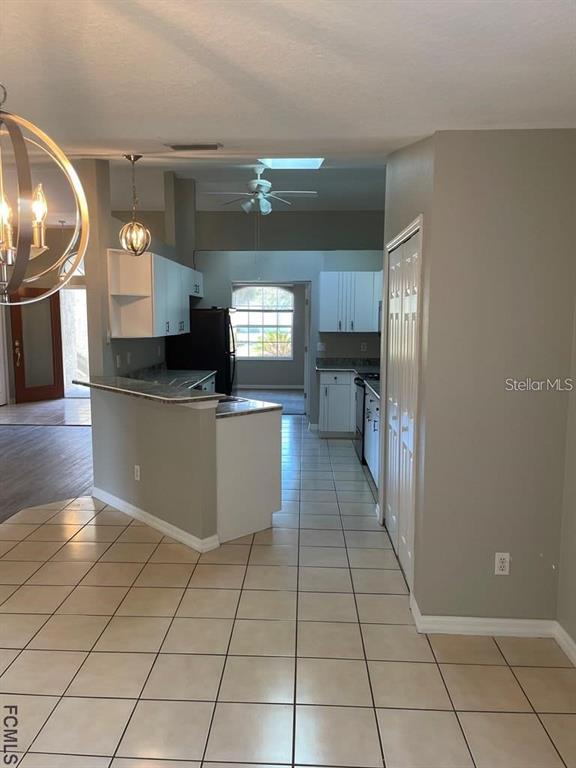 A kitchen with white cabinets, a breakfast bar, and tile flooring opens to a dining area — 61 FRANCISCAN LANE, PALM COAST, FL