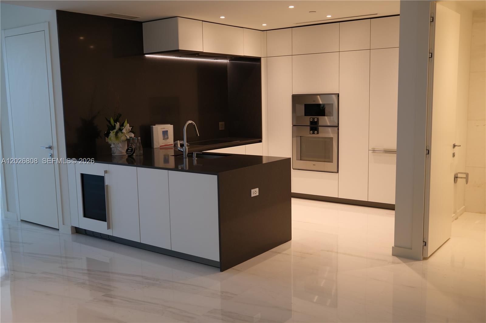 A modern kitchen features white cabinetry, dark countertops, stainless steel appliances, and marble flooring — 300 Biscayne Boulevard Way # 2509W, Miami FL 33131, MIAMI, FL