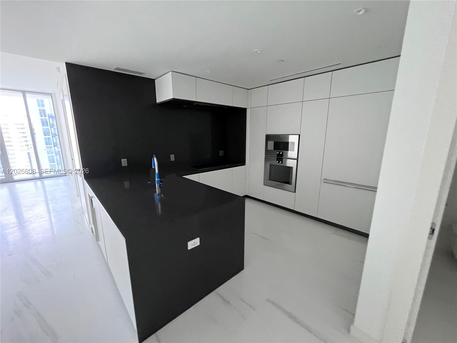 A modern kitchen features a black island, dark countertops, and white cabinetry — 300 Biscayne Boulevard Way # 2509W, Miami FL 33131, MIAMI, FL