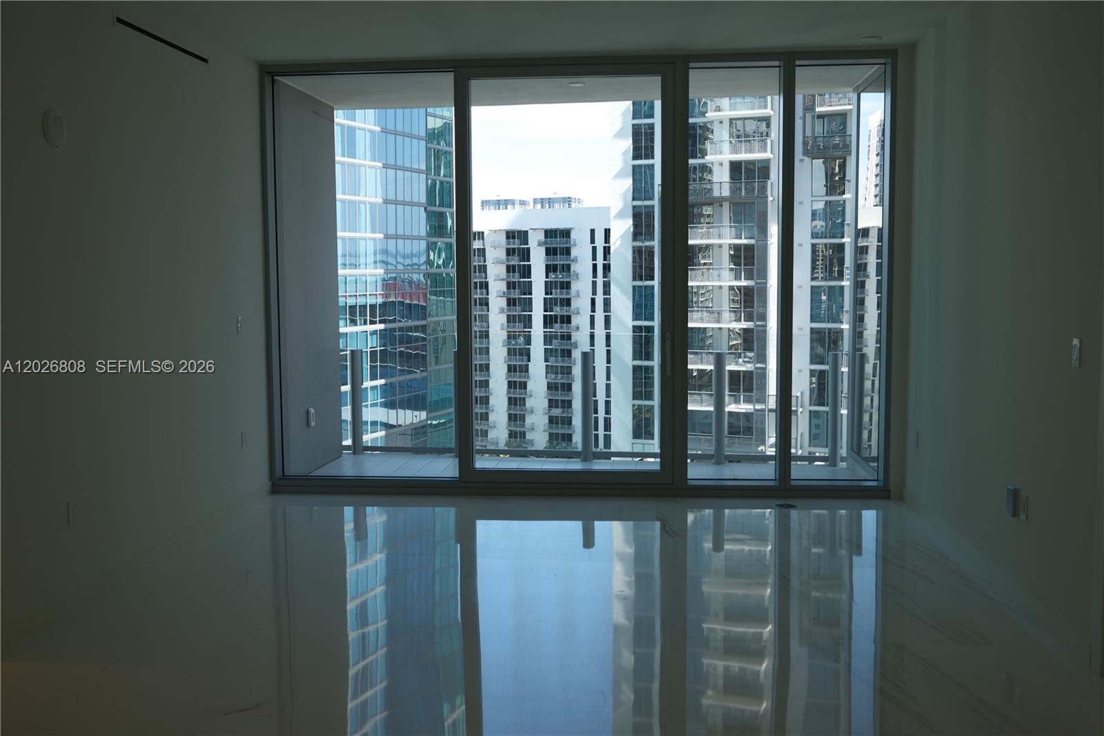 A room with polished white floors features floor-to-ceiling windows overlooking urban high-rise buildings — 300 Biscayne Boulevard Way # 2509W, Miami FL 33131, MIAMI, FL