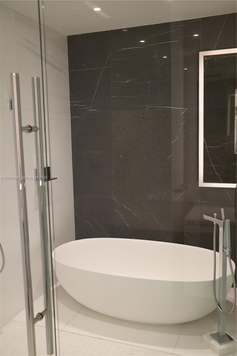 A modern bathroom features a freestanding white bathtub against a dark marble accent wall — 300 Biscayne Boulevard Way # 2509W, Miami FL 33131, MIAMI, FL