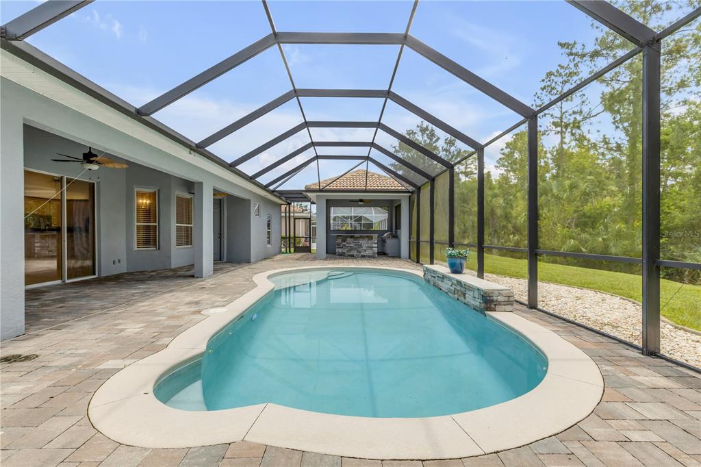 A screened-in patio features a swimming pool with a stone water feature and outdoor kitchen — 3550 GRANDE TUSCANY WAY, NEW SMYRNA BEACH, FL
