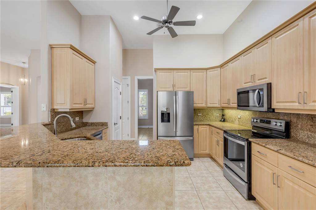 A kitchen features light wood cabinets, granite countertops, stainless steel appliances, and tile flooring — 3550 GRANDE TUSCANY WAY, NEW SMYRNA BEACH, FL