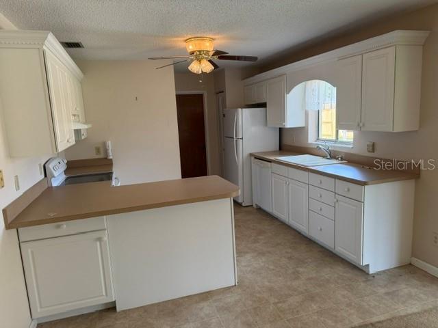 A kitchen features white cabinets, tan countertops, a white refrigerator, and a ceiling fan — 3048 UNITY TREE DRIVE, EDGEWATER, FL