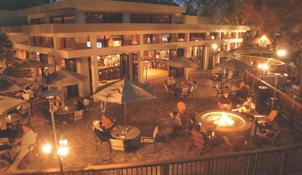 An outdoor patio at night features a fire pit, dining tables, and a modern building — 1602 SANDHILL COURT, PALM HARBOR, FL