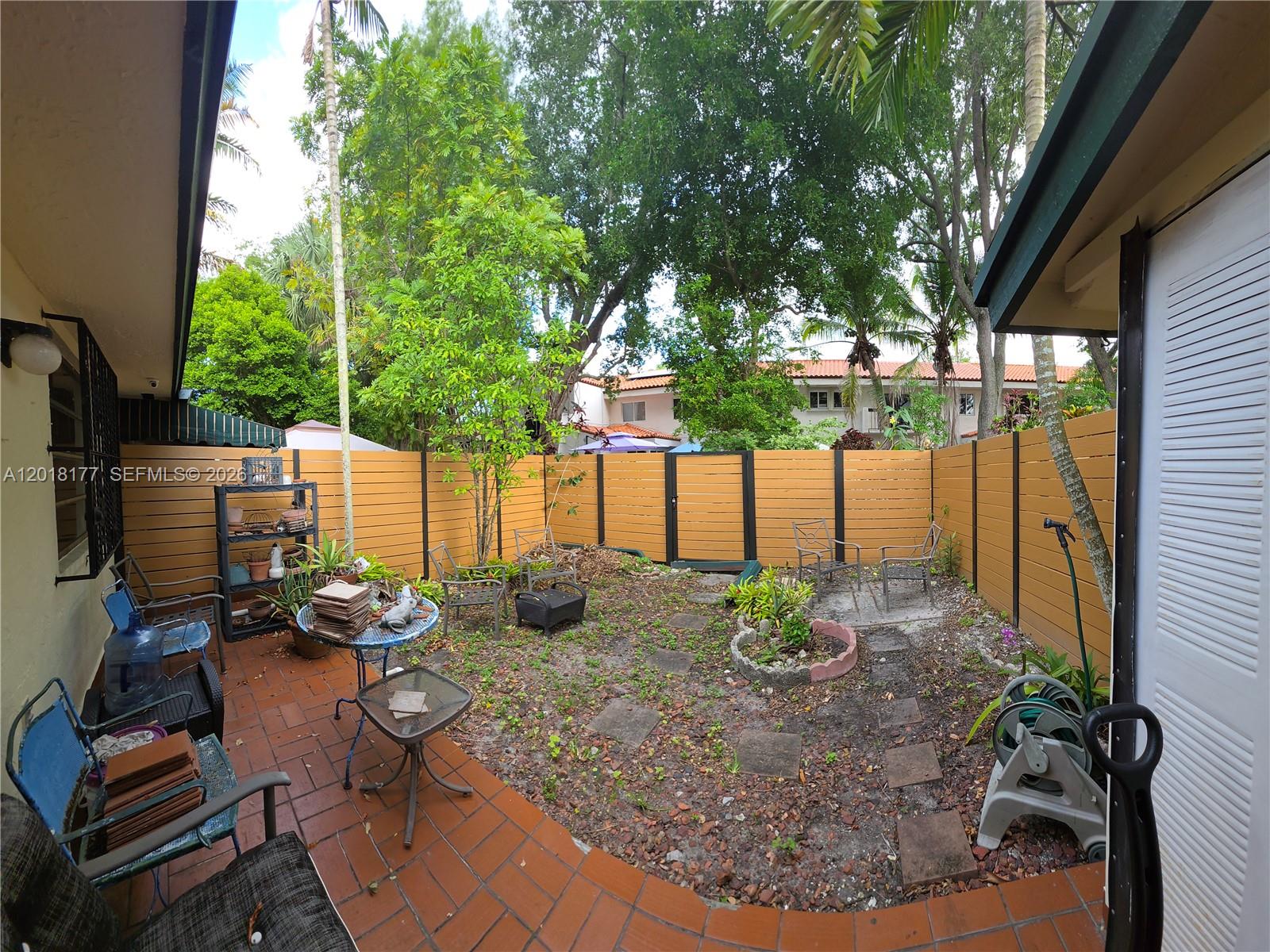 A small backyard features a brick patio, a wooden fence, and scattered stone pavers — 10908 SW 72nd St # 215, Miami FL 33173, MIAMI, FL