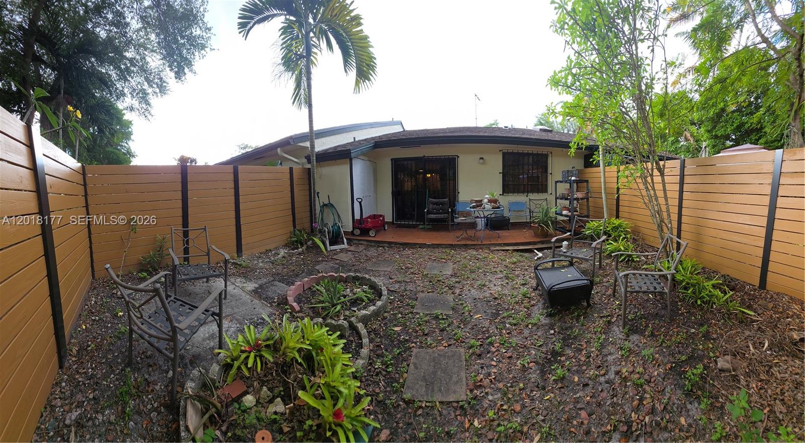 A fenced backyard features a patio, scattered chairs, a small garden bed, and palm trees — 10908 SW 72nd St # 215, Miami FL 33173, MIAMI, FL