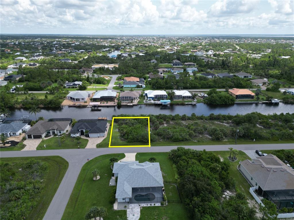 An aerial view shows a vacant, rectangular waterfront lot outlined in yellow along a street — 15120 HENNIPEN CIRCLE, PORT CHARLOTTE, FL