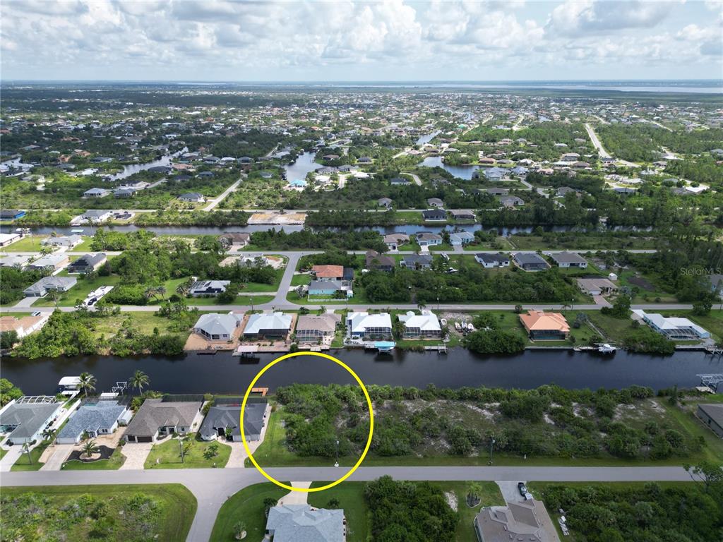 An aerial view shows a vacant, wooded waterfront lot circled in yellow next to a house — 15120 HENNIPEN CIRCLE, PORT CHARLOTTE, FL