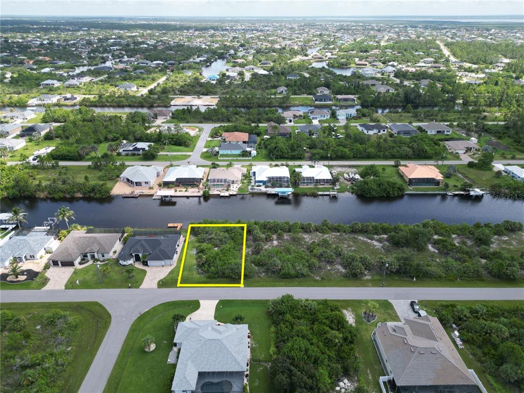 An aerial view shows a vacant, rectangular waterfront lot outlined in yellow — 15120 HENNIPEN CIRCLE, PORT CHARLOTTE, FL