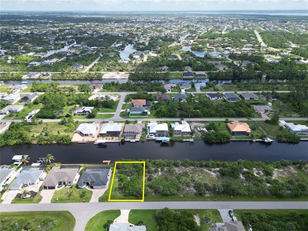 An aerial view shows a vacant, rectangular waterfront lot highlighted in yellow along a canal — 15120 HENNIPEN CIRCLE, PORT CHARLOTTE, FL