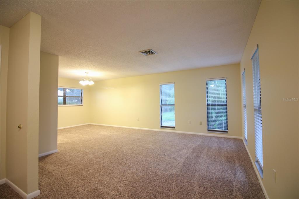 An empty living room features beige carpeting, light yellow walls, and several windows with blinds — 2014 CHARNES DRIVE, LAKELAND, FL