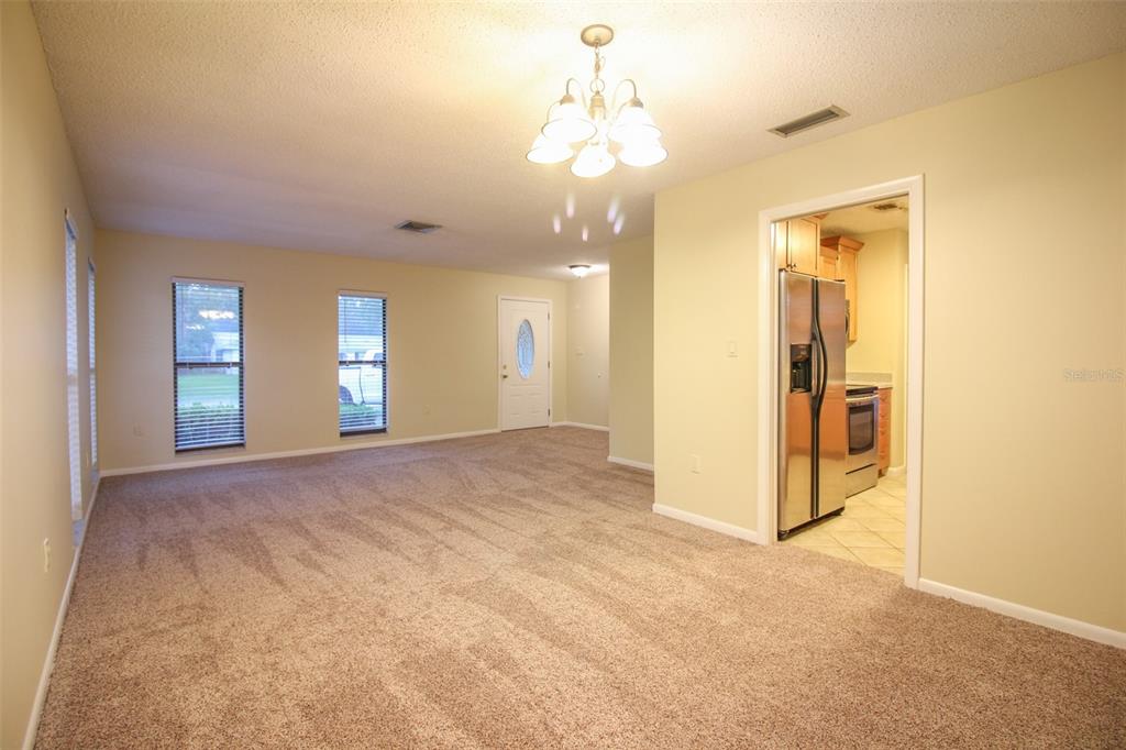 A carpeted living room features a chandelier, two windows, and a doorway to a kitchen — 2014 CHARNES DRIVE, LAKELAND, FL
