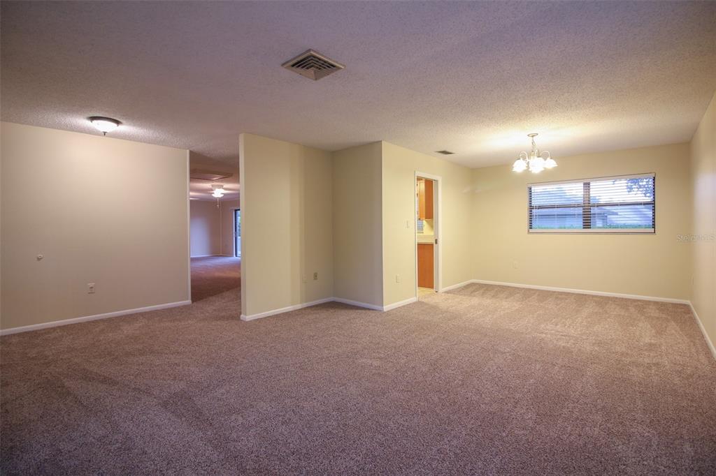 A carpeted living and dining area features beige walls, a chandelier, and a ceiling vent — 2014 CHARNES DRIVE, LAKELAND, FL