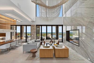 A modern living room features a large stone fireplace, a beaded chandelier, and floor-to-ceiling windows — VERO BEACH, FL