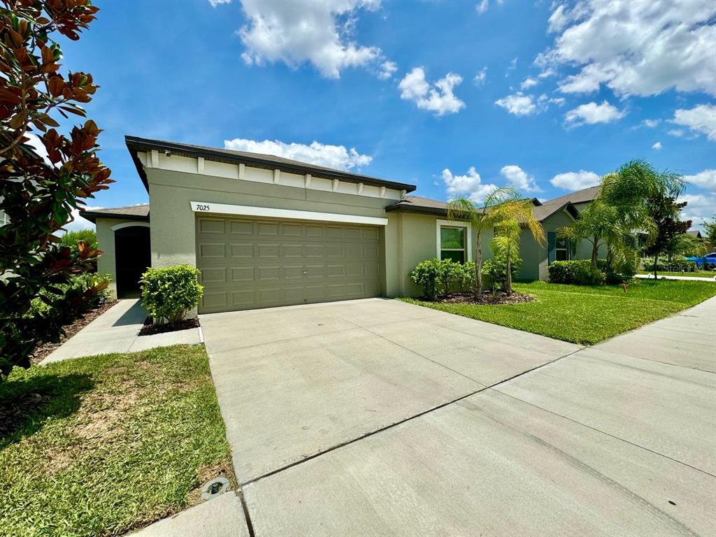 A single-story house with a tan stucco exterior, a two-car garage, and a concrete driveway — 7025 KING CREEK DRIVE, SUN CITY CENTER, FL