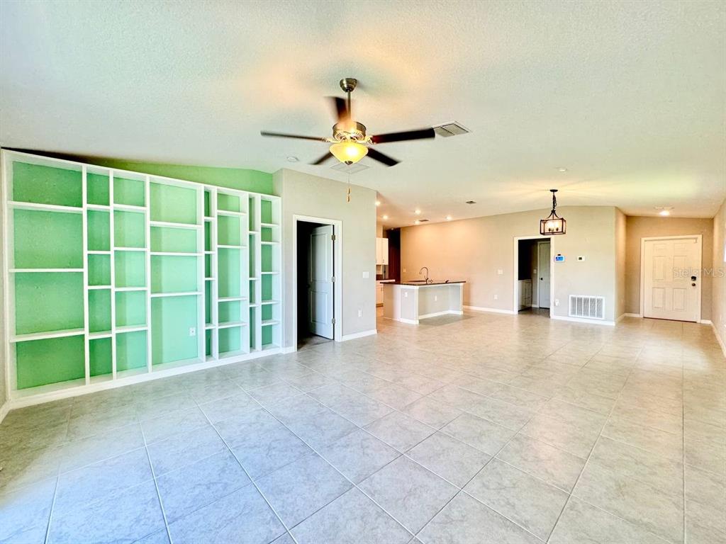 A spacious living room features light tile flooring, a large mint-green built-in bookshelf, and a kitchen — 7025 KING CREEK DRIVE, SUN CITY CENTER, FL