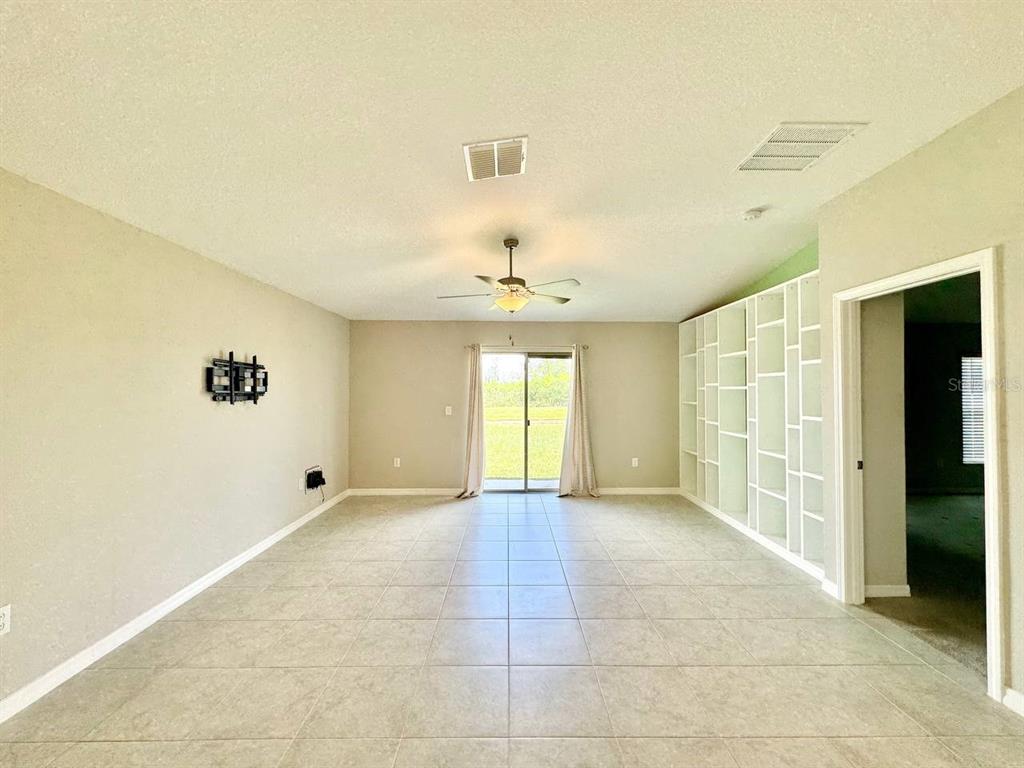 A spacious living room features tile flooring, a ceiling fan, and built-in white shelving — 7025 KING CREEK DRIVE, SUN CITY CENTER, FL
