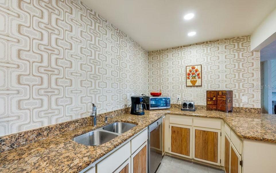 A kitchen features patterned wallpaper, granite countertops, wood-accented cabinets, and stainless steel appliances — 1286 JOHN ANDERSON DRIVE, ORMOND BEACH, FL