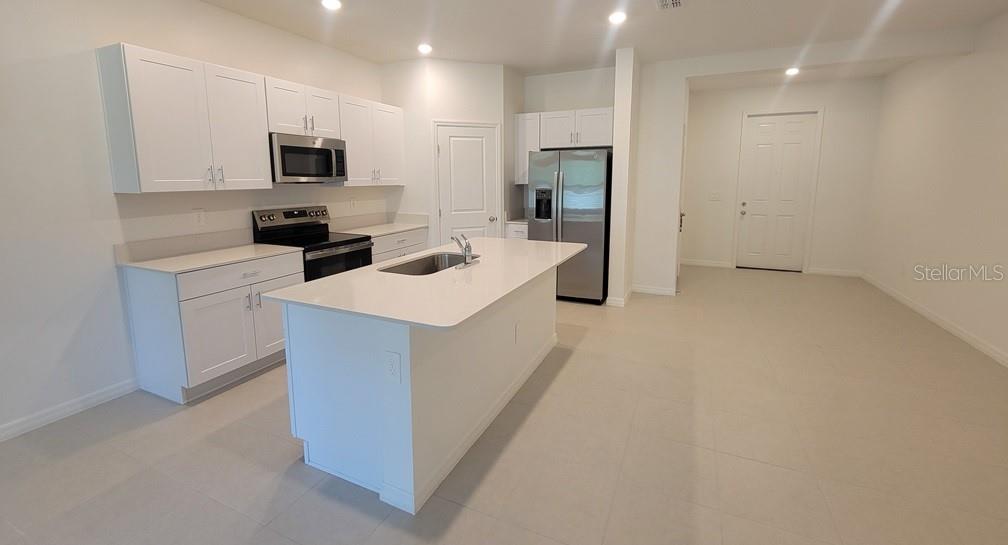 A modern kitchen features white cabinets, stainless steel appliances, and a central island with sink — 3328 LAPIS LAKE DRIVE, ZEPHYRHILLS, FL