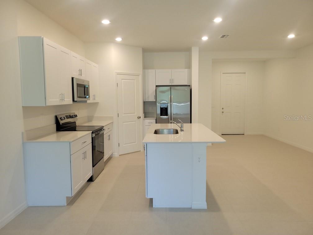 A modern kitchen features white cabinets, stainless steel appliances, and a central island with seating — 3328 LAPIS LAKE DRIVE, ZEPHYRHILLS, FL