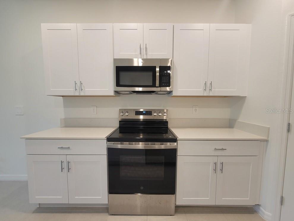 A kitchen features white cabinets, stainless steel appliances, and light-colored countertops — 3328 LAPIS LAKE DRIVE, ZEPHYRHILLS, FL