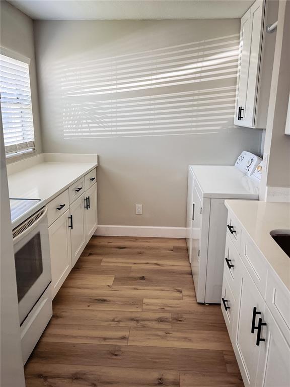 A laundry room features white cabinets, quartz countertops, a washer, and wood-look flooring — 24862 US HIGHWAY 19 N UNIT 1602, CLEARWATER, FL