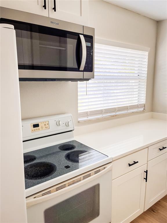 A kitchen features a white electric stove, a stainless steel microwave, and white cabinetry — 24862 US HIGHWAY 19 N UNIT 1602, CLEARWATER, FL