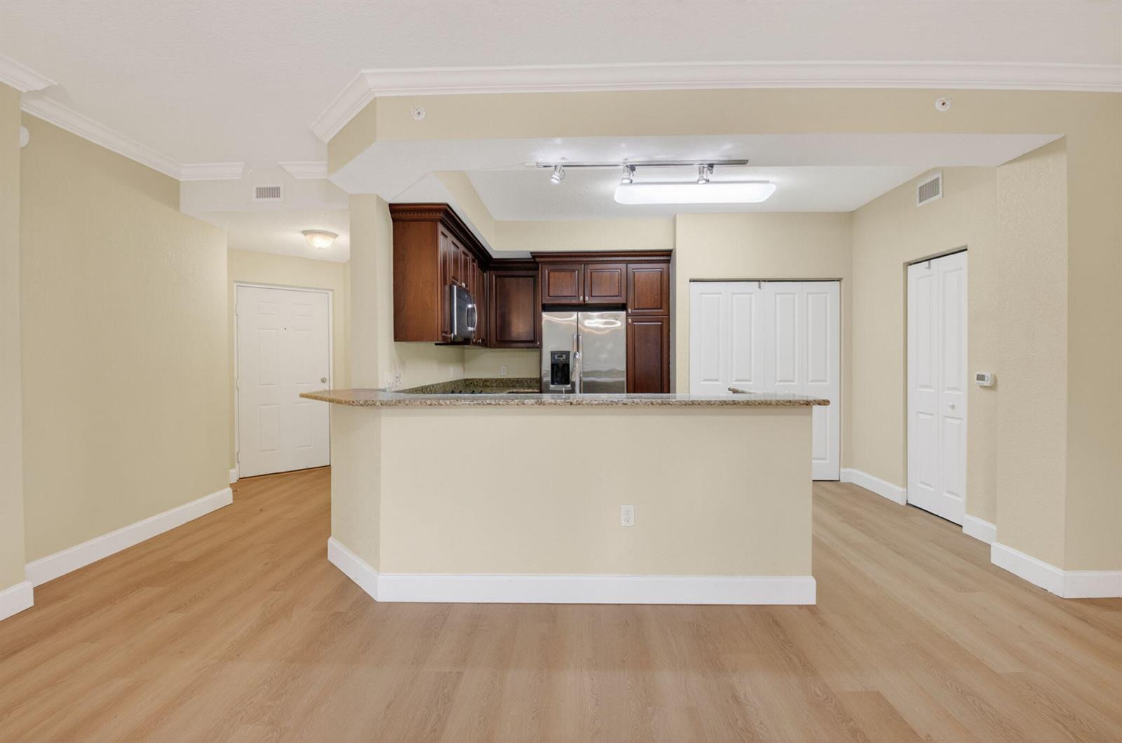 A kitchen with dark wood cabinets and a granite breakfast bar overlooks an open room — 1690 Renaissance Commons Boulevard # 1219, Boynton Beach FL 33426, BOYNTON BEACH, FL