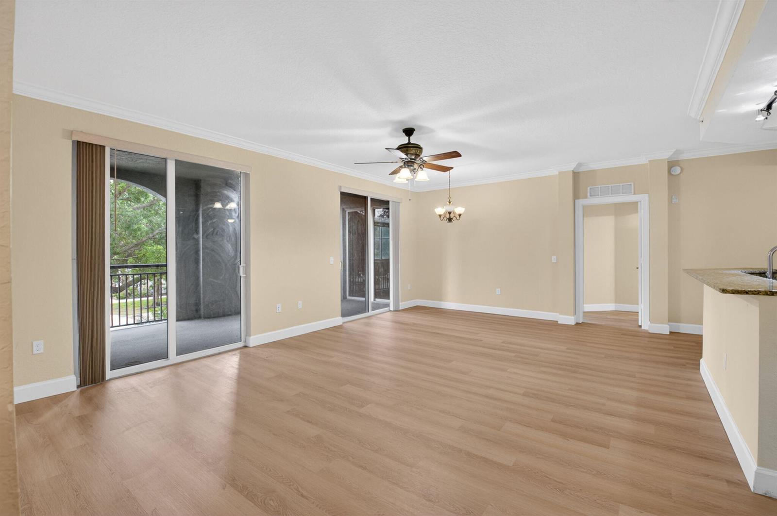 An empty living room with light wood flooring, beige walls, a ceiling fan, and sliding doors — 1690 Renaissance Commons Boulevard # 1219, Boynton Beach FL 33426, BOYNTON BEACH, FL