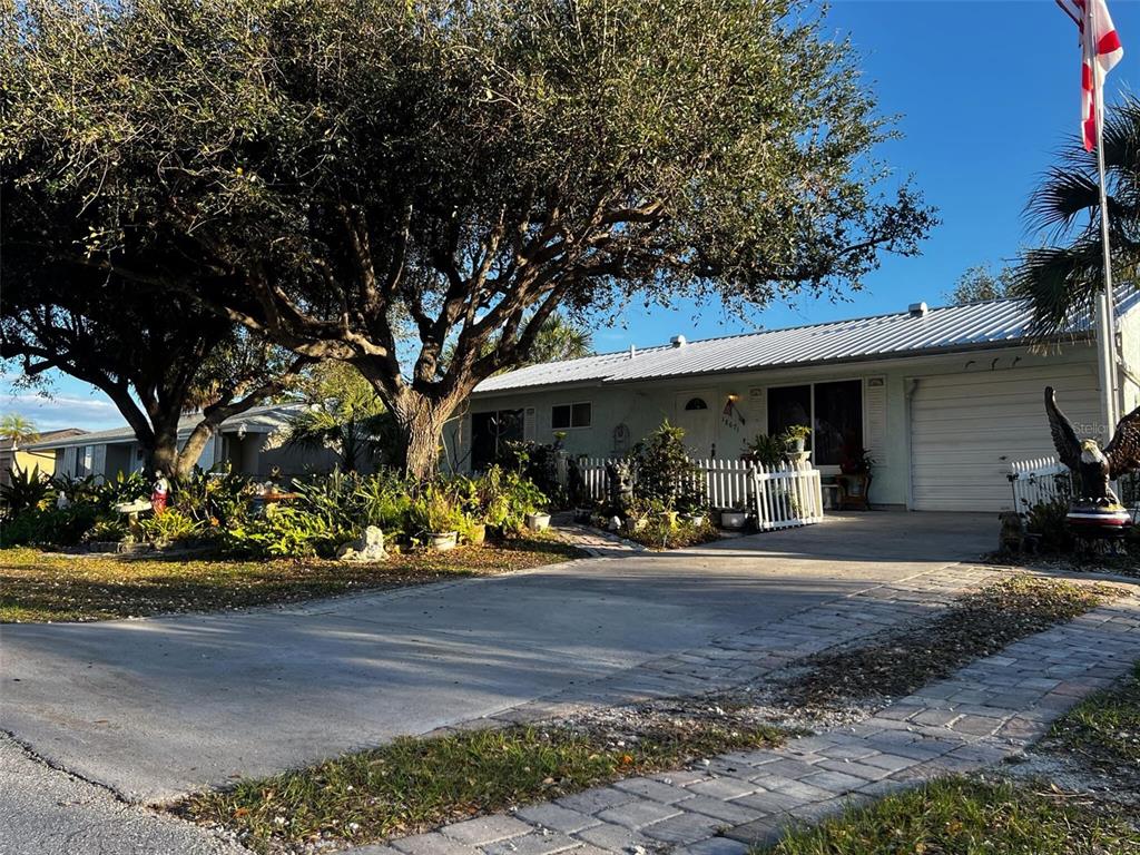 A single-story house with a metal roof, a large tree, and a paved driveway — 18671 KERRVILLE CIRCLE, PORT CHARLOTTE, FL