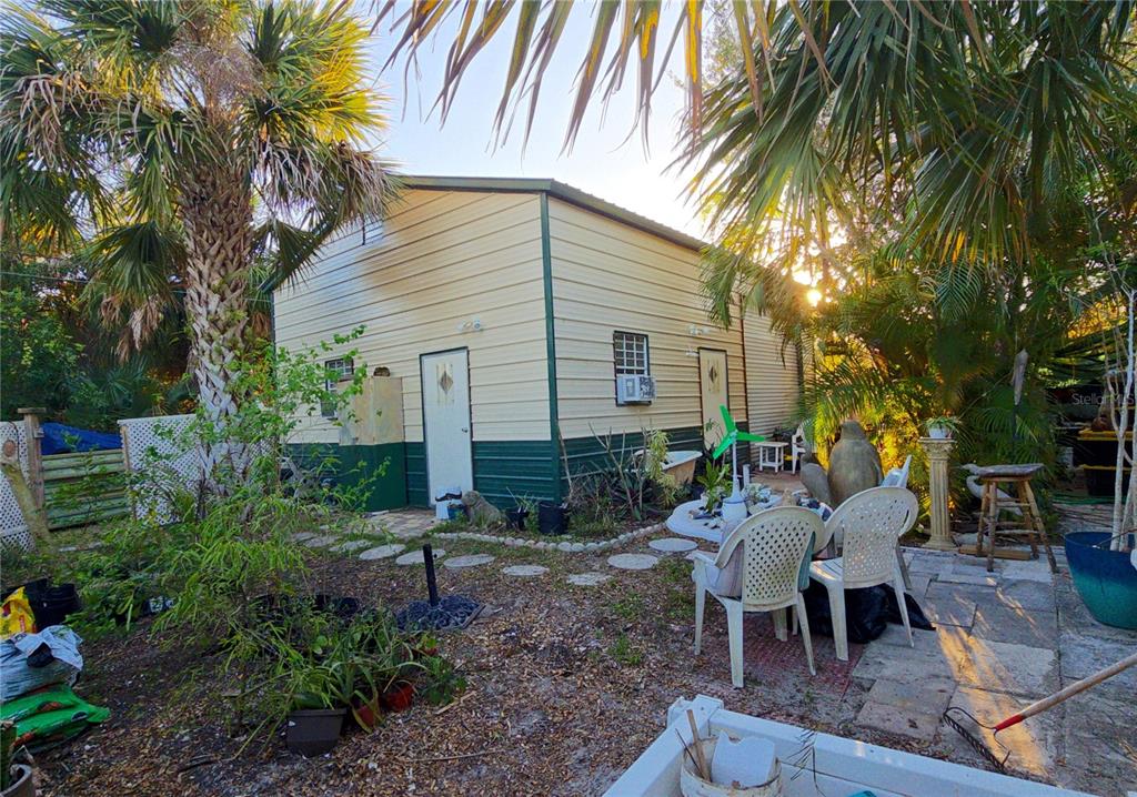 A detached metal-sided building sits in a backyard with a patio, chairs, and palm trees — 18671 KERRVILLE CIRCLE, PORT CHARLOTTE, FL