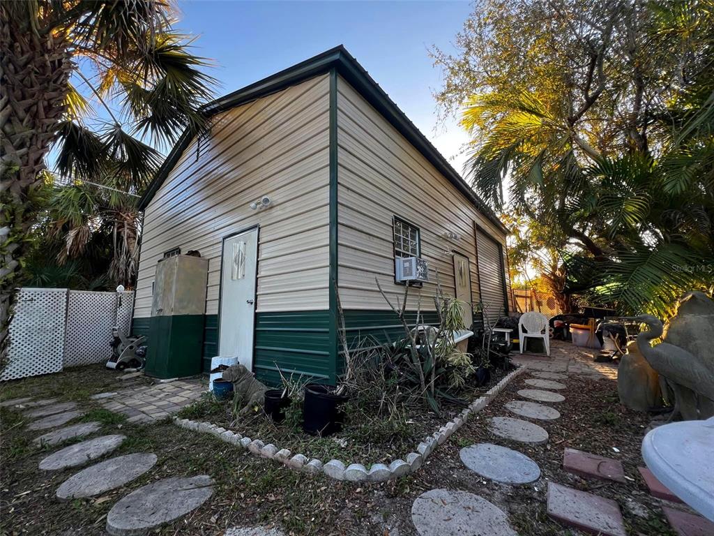 A small, metal-sided shed with a green base sits in a yard with palm trees — 18671 KERRVILLE CIRCLE, PORT CHARLOTTE, FL