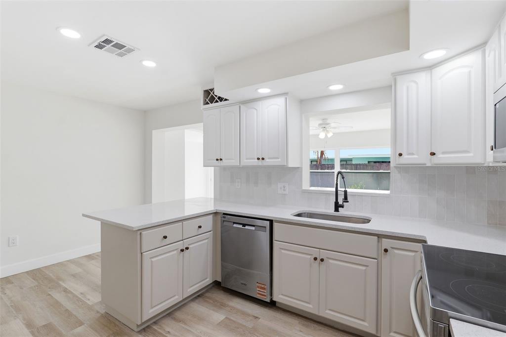 A kitchen features white cabinets, stainless steel appliances, a sink, and light-colored wood flooring — 524 WESTMINSTER AVENUE, MELBOURNE, FL