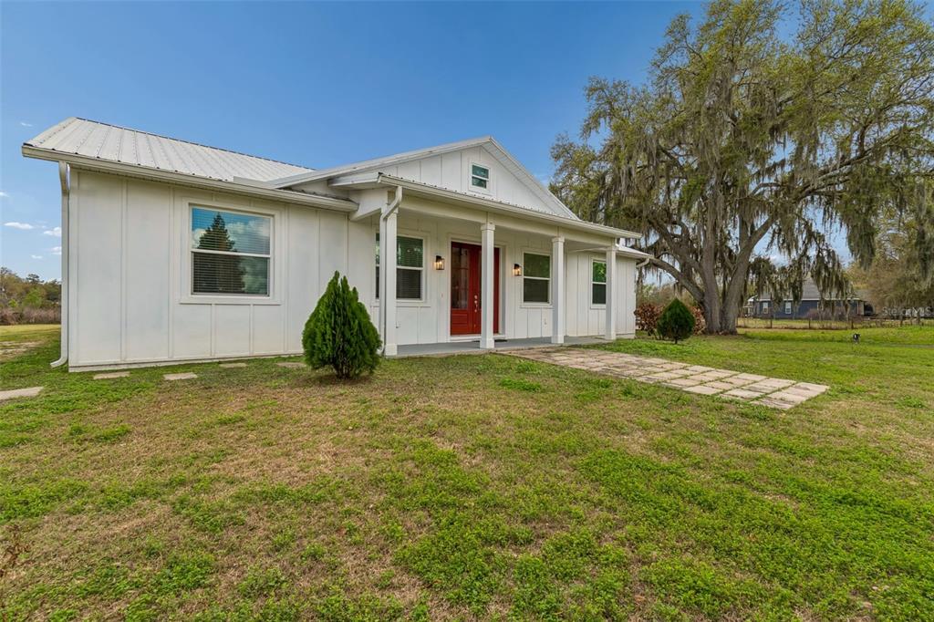 A white farmhouse-style home with a metal roof, red front door, and a covered porch — 5614 PLESS ROAD, PLANT CITY, FL