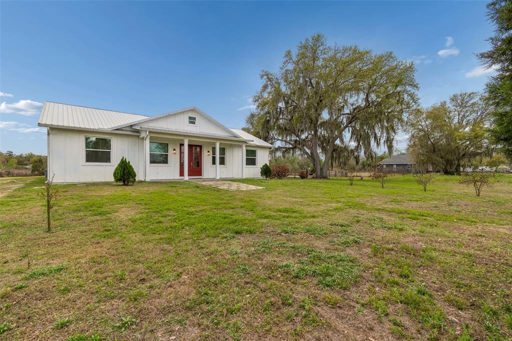 A white farmhouse with a metal roof and a red front door sits on grass — 5614 PLESS ROAD, PLANT CITY, FL