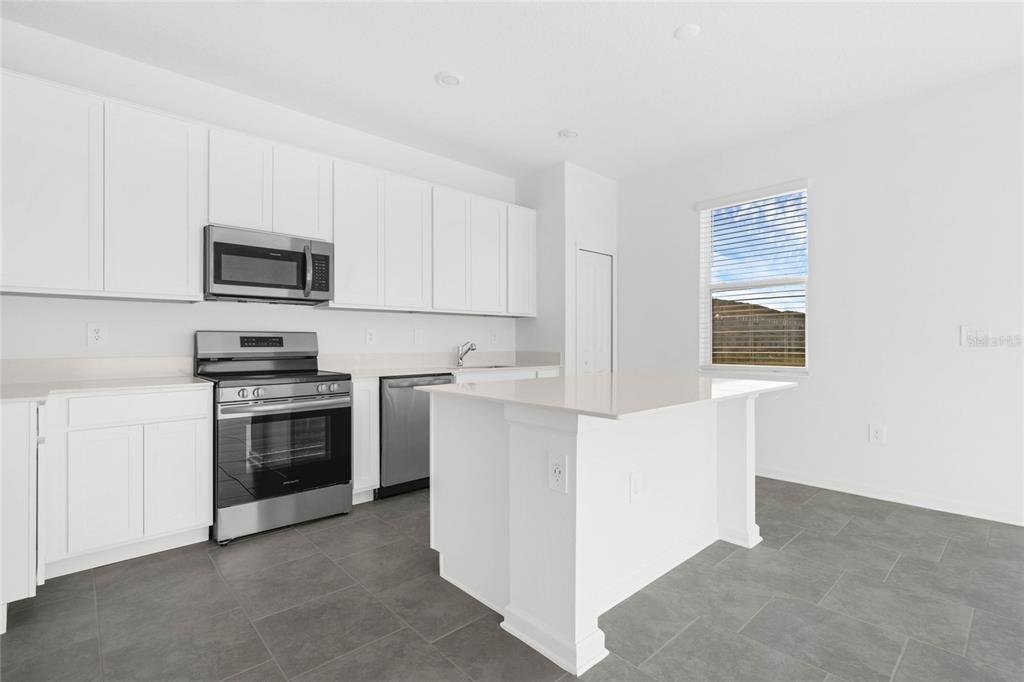 A modern kitchen features white cabinets, stainless steel appliances, a center island, and gray flooring — 2788 PIERR STREET, DAVENPORT, FL