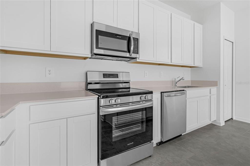 A kitchen features white cabinets, stainless steel appliances, and light-colored countertops over gray tile flooring — 2788 PIERR STREET, DAVENPORT, FL