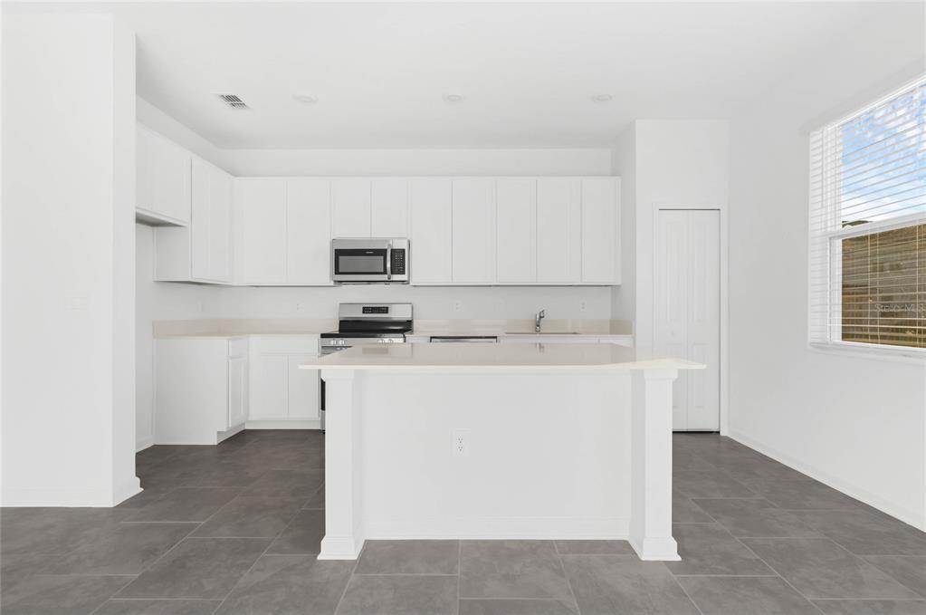 A modern kitchen features white cabinetry, stainless steel appliances, a center island, and gray tile — 2788 PIERR STREET, DAVENPORT, FL