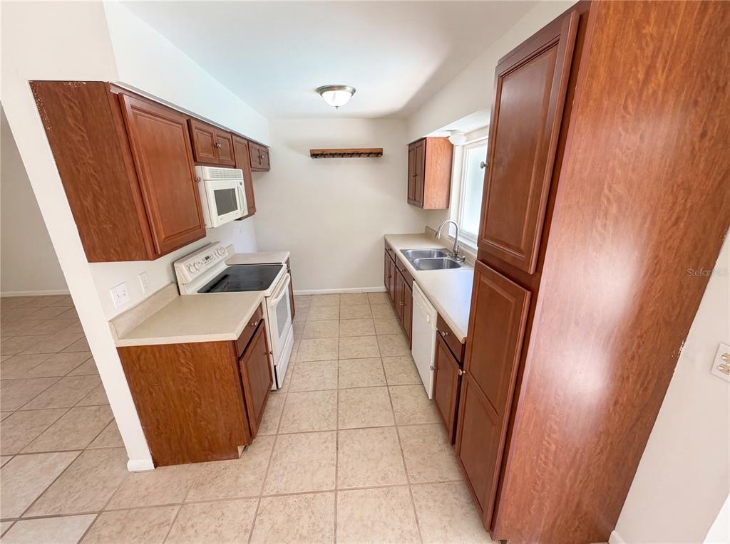 A galley kitchen features wood cabinets, laminate countertops, a white stove, and tile flooring — 909 WINCHESTER COURT, BRANDON, FL