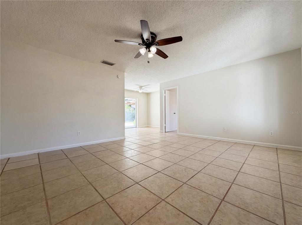 A spacious room with light-colored walls, tan tile flooring, and a ceiling fan — 909 WINCHESTER COURT, BRANDON, FL