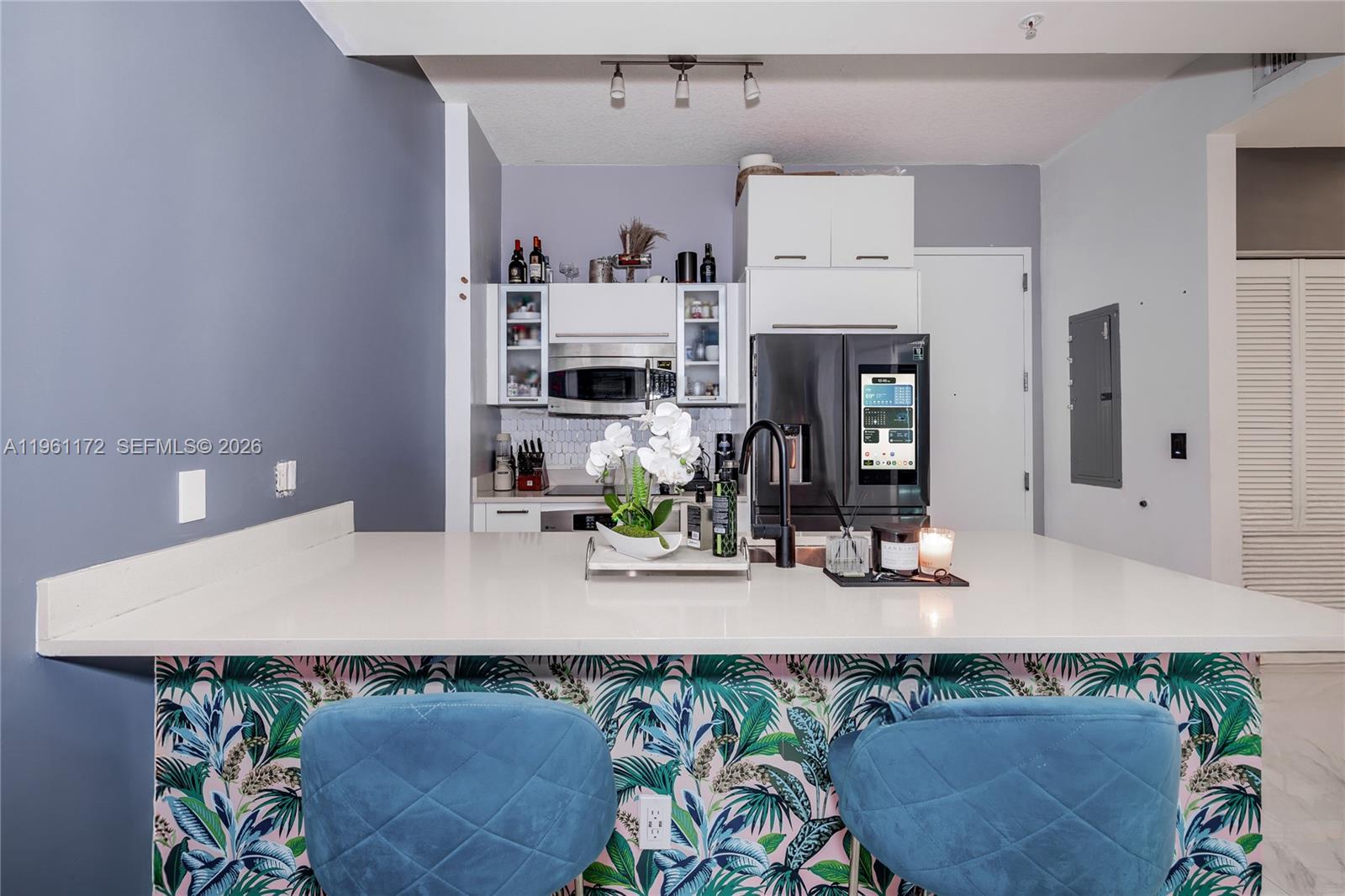 A kitchen features a white countertop island with blue velvet stools and tropical-patterned wallpaper — 333 NE 24th St # 1912, Miami FL 33137, MIAMI, FL