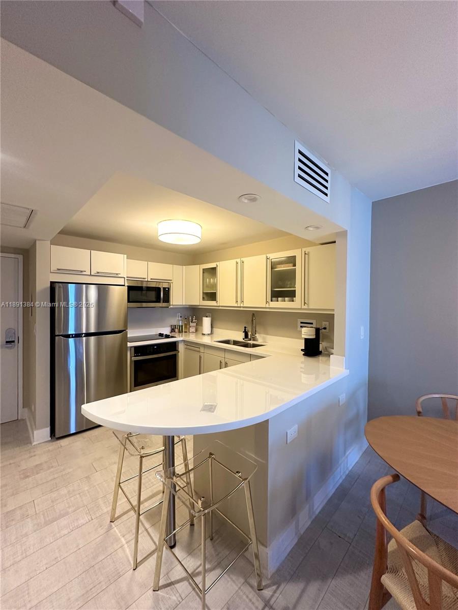 A kitchen features white cabinetry, stainless steel appliances, and a peninsula with bar seating — 2301 Collins Ave # 836, Miami Beach FL 33139, MIAMI BEACH, FL