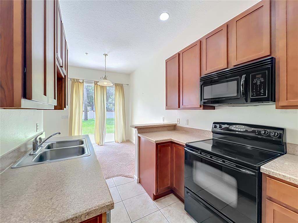 A kitchen with wood cabinets, black appliances, laminate countertops, and a view of the backyard — 600 NORTHERN WAY UNIT 1804, WINTER SPRINGS, FL
