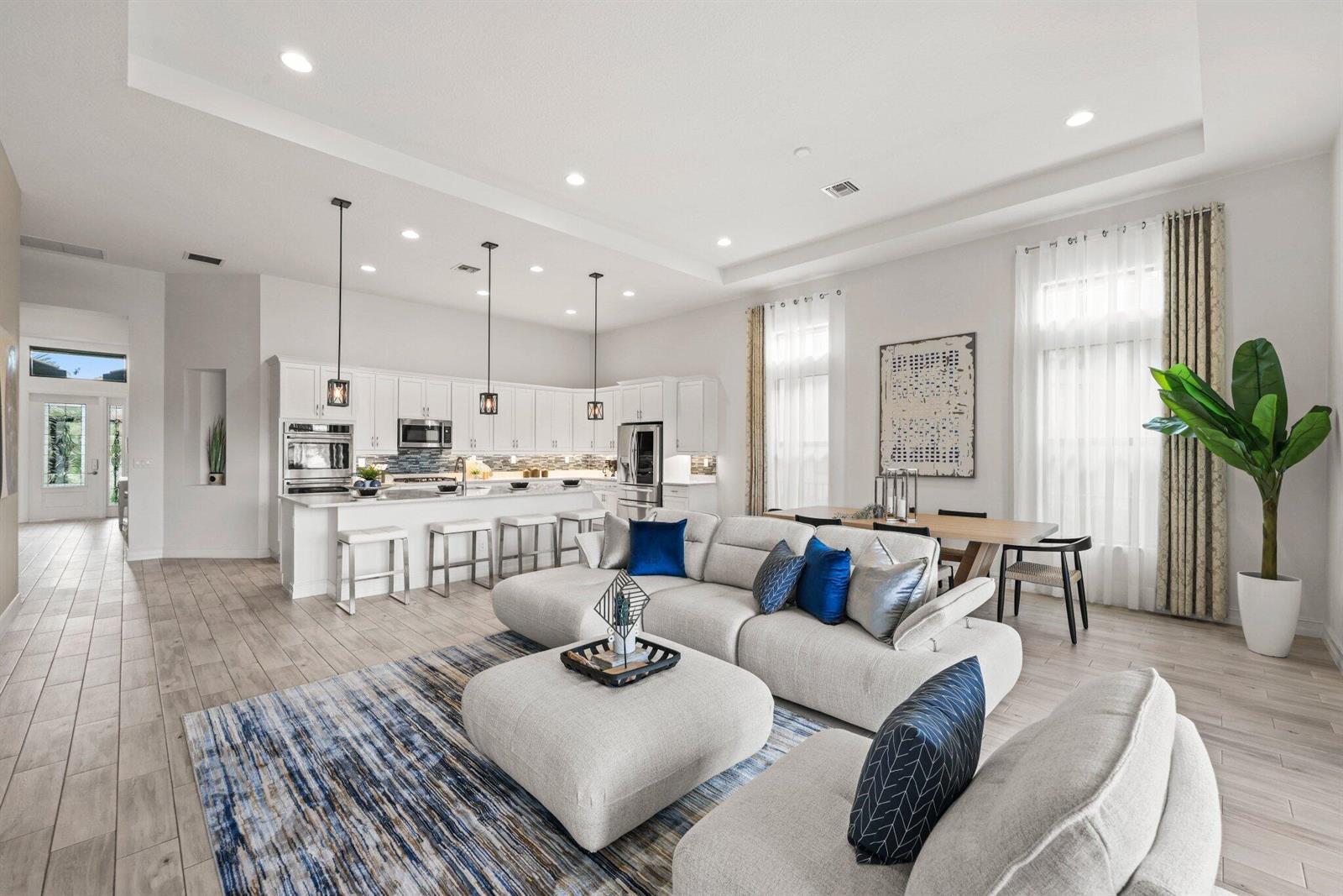 An open-concept living room and kitchen featuring light wood floors, white cabinetry, and blue accents — 11856 Leon Circle N, Parkland FL 33076, PARKLAND, FL
