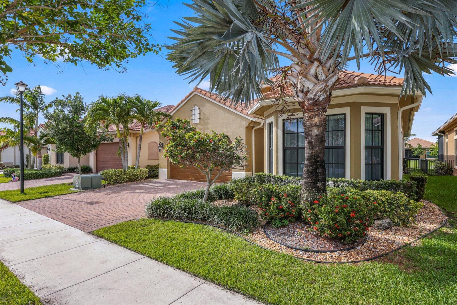 A single-story stucco house with a tile roof, brick driveway, and palm trees in front — 11856 Leon Circle N, Parkland FL 33076, PARKLAND, FL