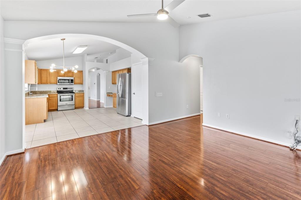 A kitchen with light wood cabinets and stainless steel appliances opens to a hardwood-floored room — 5417 ALGERINE PL, WESLEY CHAPEL, FL