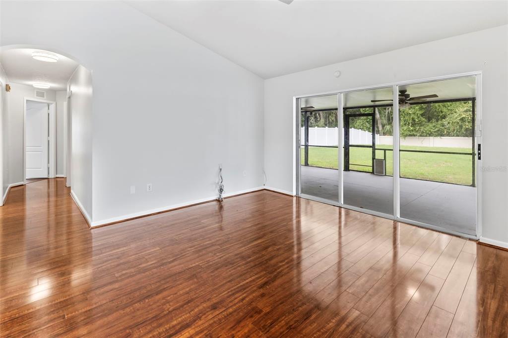 An empty room with hardwood floors, white walls, and sliding glass doors leading to a patio — 5417 ALGERINE PL, WESLEY CHAPEL, FL