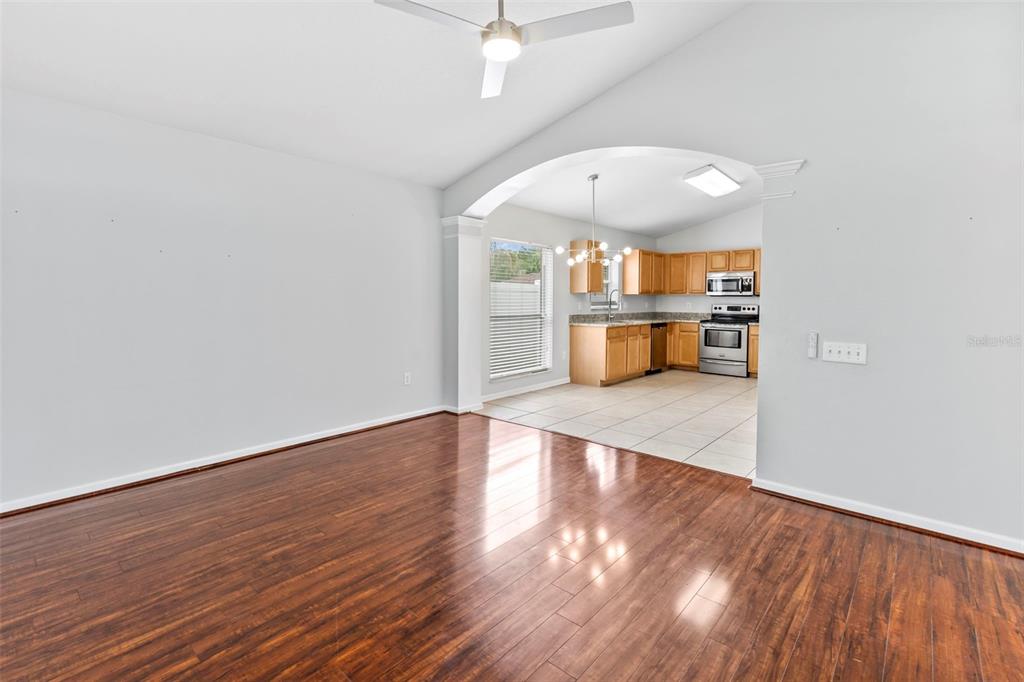 A living room with wood flooring leads through an arched opening into a tiled kitchen — 5417 ALGERINE PL, WESLEY CHAPEL, FL
