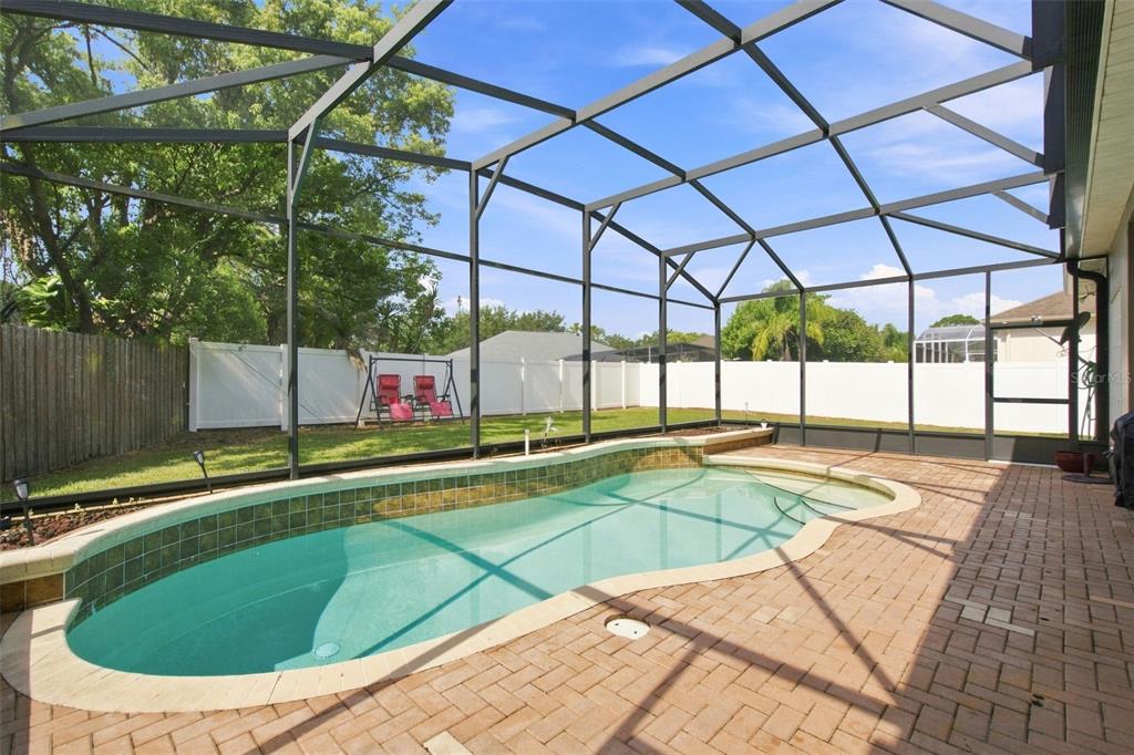A screened-in patio features a kidney-shaped swimming pool and brick pavers in a fenced backyard — 13711 DORNOCH DRIVE, ORLANDO, FL